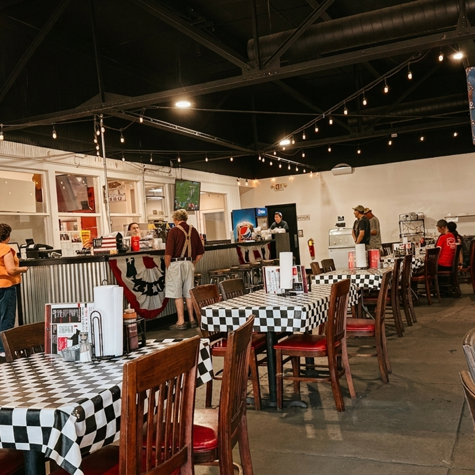 Casual restaurant interior with checkered tablecloths, people at the counter, and vintage signs.